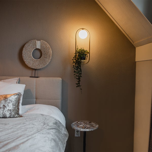 Schlafzimmer mit Bett, Wanddekoration und Wandleuchte mit Pflanze
