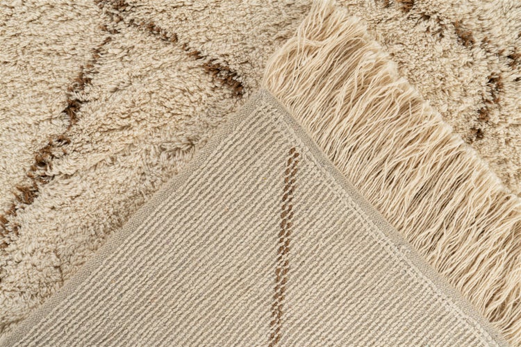 Detailansicht eines Hochflor-Teppichs mit Fransen und dunkelbraunem Muster, zeigt die flauschige Oberfläche und die gewebte Rückseite.