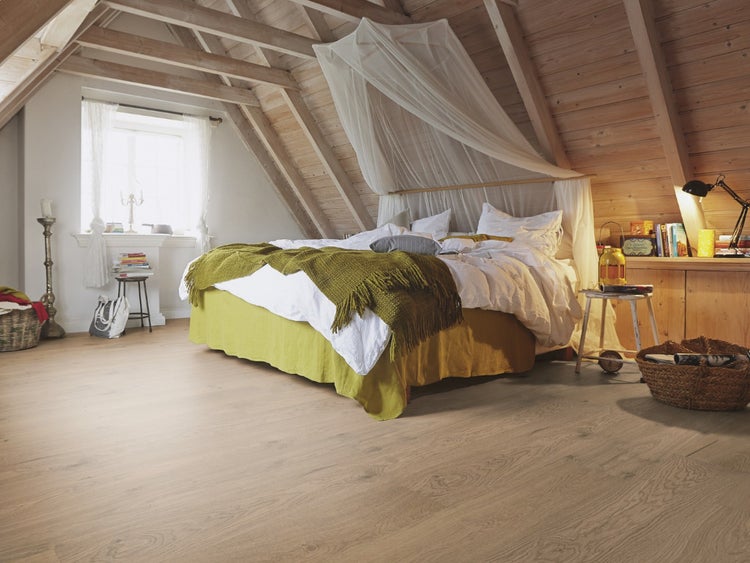 Rustikales Schlafzimmer unter einer Dachschräge mit hellem Holzboden, Holzbalken an der Decke und einem großen Bett mit Betthimmel.