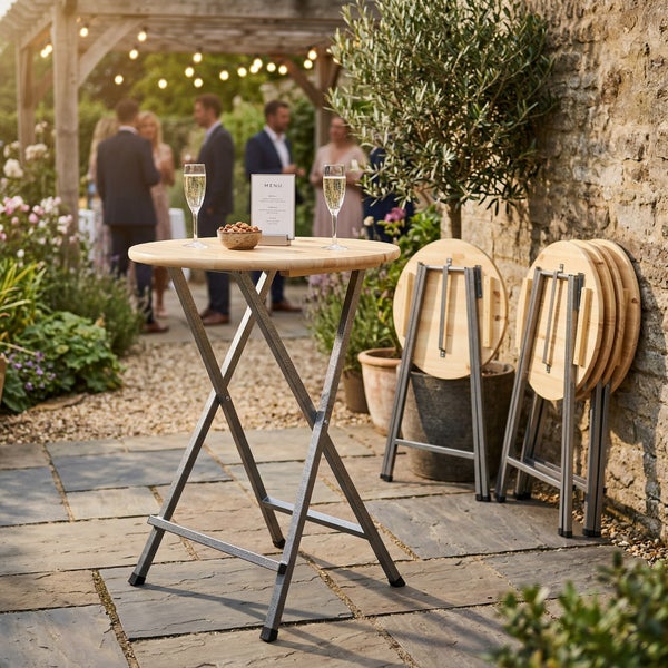 Klappbarer Stehtisch mit runder Holzplatte und grauem Metallgestell auf einer festlich dekorierten Steinterrasse im Freien.