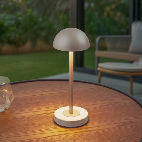 Moderne LED Tischleuchte mit pilzförmigem Schirm und Marmorfuß auf einem hölzernen Gartentisch bei Dämmerung.