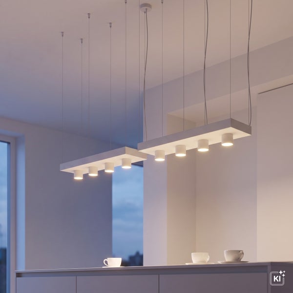 Zwei moderne längliche Pendelleuchten mit mehreren LED Strahlern über einem Küchentresen mit Kaffeetassen in einem hellen, minimalistischen Raum.