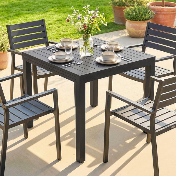 Modernes Gartenmöbel-Set aus anthrazitfarbenem Metall mit einem quadratischen Tisch und vier Armlehnstühlen auf einer hellen Terrasse.