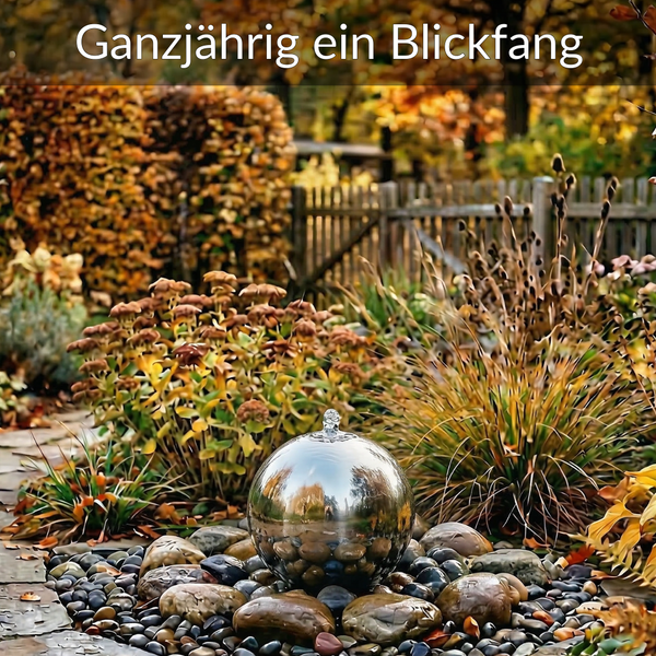 Edelstahl-Kugelbrunnen auf Flusssteinen in einem organisierten Garten mit Gräsern und Stauden.
