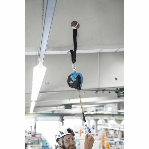 Zarges Höhensicherungsgerät an Deckenanker befestigt, Arbeiter mit Schutzhelm bedient das ausziehbare Gurtband in einem Industriebau.