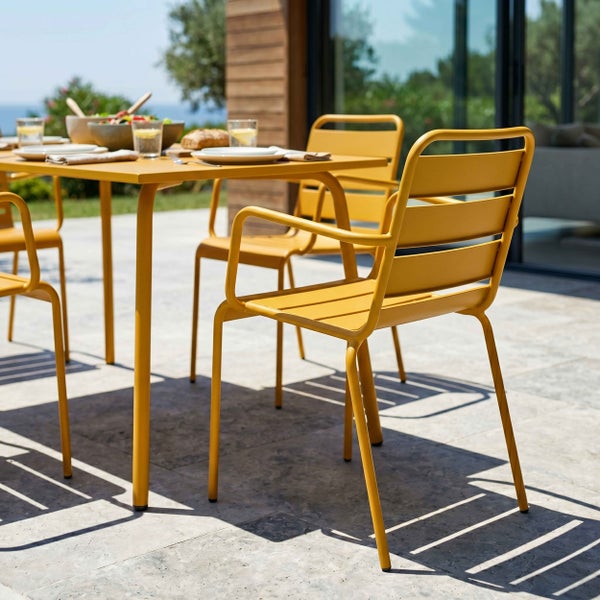 Gelbes Gartenmöbel-Set aus Metall mit einem rechteckigen Tisch und Gartenstühlen mit Armlehnen auf einer sonnigen Terrasse.