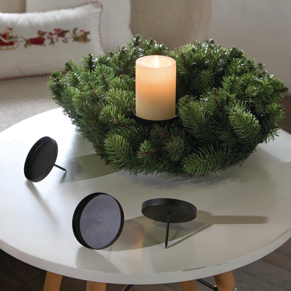 Set aus vier schwarzen Kerzenhaltern zum Einstecken in einen Adventskranz mit einer brennenden Stumpenkerze auf einem runden Tisch.