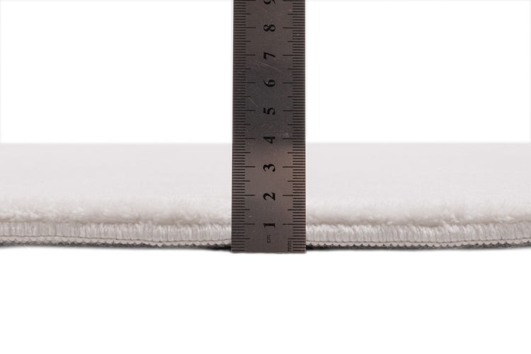 Weißer Teppich mit weicher Oberfläche, dessen Florhöhe von etwa einem Zentimeter mit einem Lineal gemessen wird.
