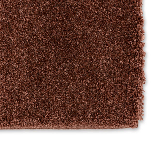 Nahaufnahme eines braunen Hochflor-Teppichs mit dichter Struktur und eingefasstem Rand.
