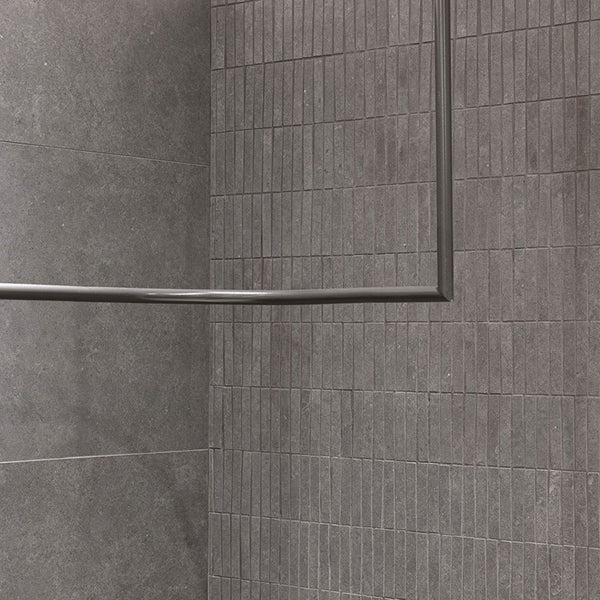 Duschstange in Eckform montiert vor Fliesenwand mit unterschiedlichen Fliesenformaten im Badezimmer.