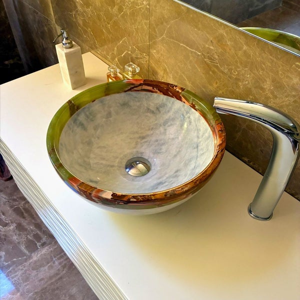 Rundes Aufsatzwaschbecken aus Glas mit buntem Muster auf weißem Waschtisch neben einer verchromten Armatur.