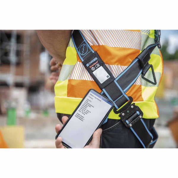 Zarges Auffanggurt an einer Person in Warnweste, Smartphone zeigt Produktdaten an.
