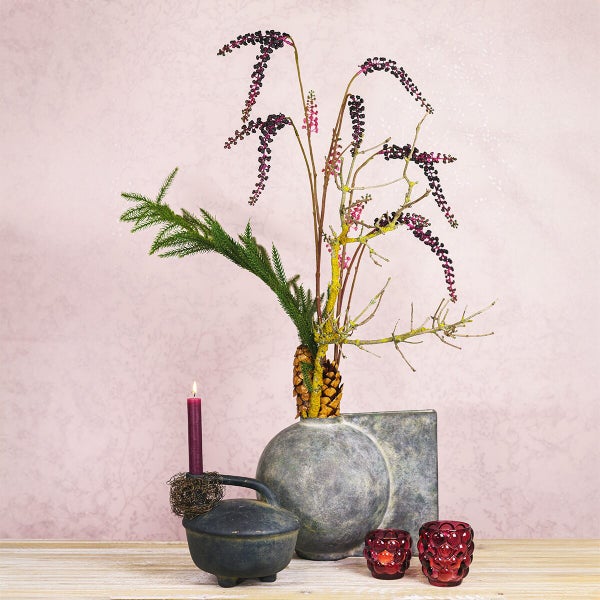 Dekoratives Arrangement mit runder Keramikvase, dunkler Schale mit Stabkerze und zwei kleinen Windlichtern auf einer Holzoberfläche.
