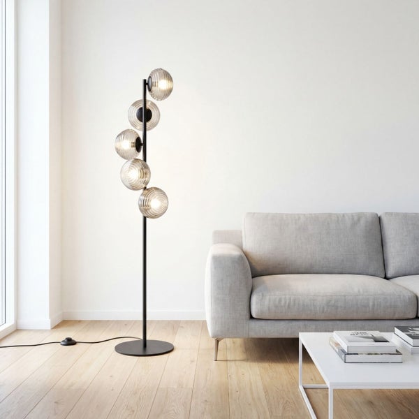 Moderne schwarze Stehleuchte mit fünf geriffelten Glaskugeln in einem hellen Wohnzimmer neben einem grauen Sofa.