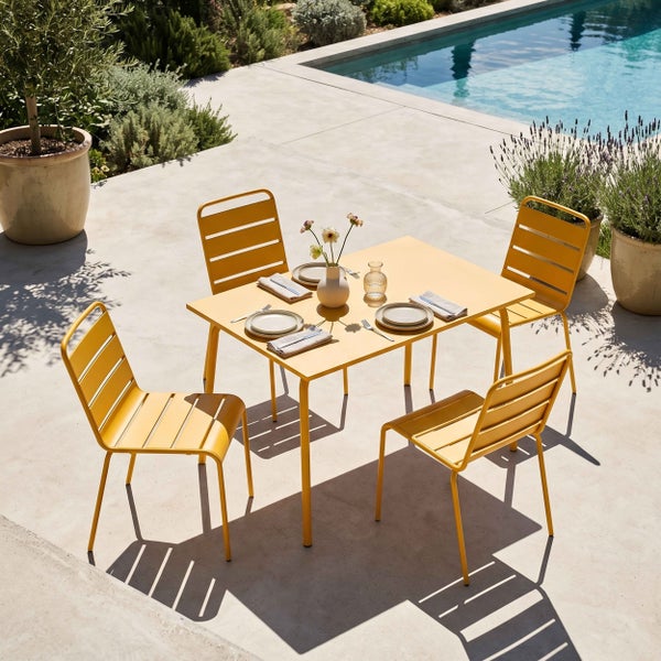 Gelbe Gartenmöbel aus Metall bestehend aus quadratischem Tisch und vier Stühlen mit Querlattung auf einer hellen Terrasse am Pool.