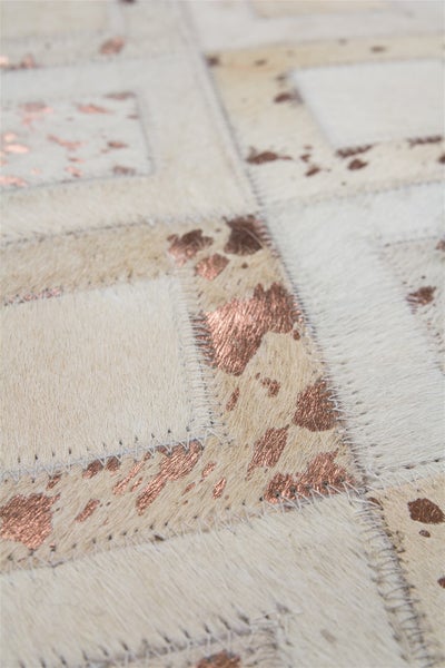 Detailansicht eines Patchwork-Teppichs aus Kuhfell mit rechteckigen Flicken, metallischen Akzenten und sichtbaren Nähten.