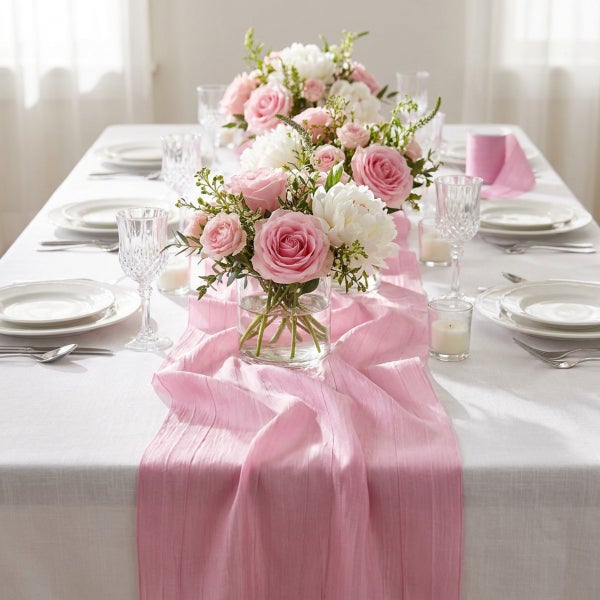 Festlich gedeckter Esstisch mit weißer Tischdecke, rosa Tischläufer, Blumenarrangements aus Rosen und Pfingstrosen sowie eleganten Gläsern.