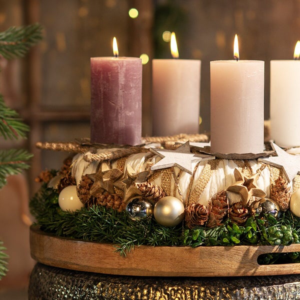 Weihnachtlicher Adventskranz mit vier Stumpenkerzen geschmückt mit Holzsternen Tannenzapfen und Weihnachtskugeln auf einem Holztablett