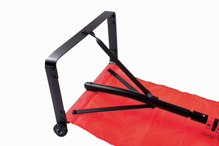 Detailansicht eines Transportwagens mit schwarzem Metallgestell, rotem Stoff und einem kleinen Rad.