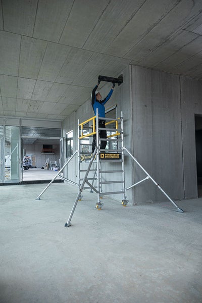 Bauarbeiter auf einem Rollgerüst bei Installationsarbeiten im Innenbereich.