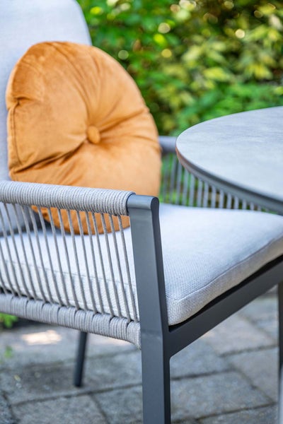 Gartenstuhl mit Seilgeflecht, Sitzkissen und rundem Zierkissen an einem runden Gartentisch im Außenbereich.