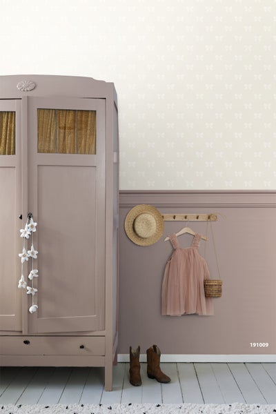 Vliestapete mit Schleifenmuster über einer Wand mit Zierleiste und passendem Schrank in einem Kinderzimmer.