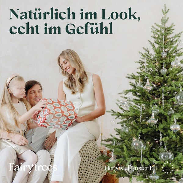 Familie beim Geschenkeauspacken neben einem naturgetreuen FairyTrees Weihnachtsbaum mit Christbaumschmuck.