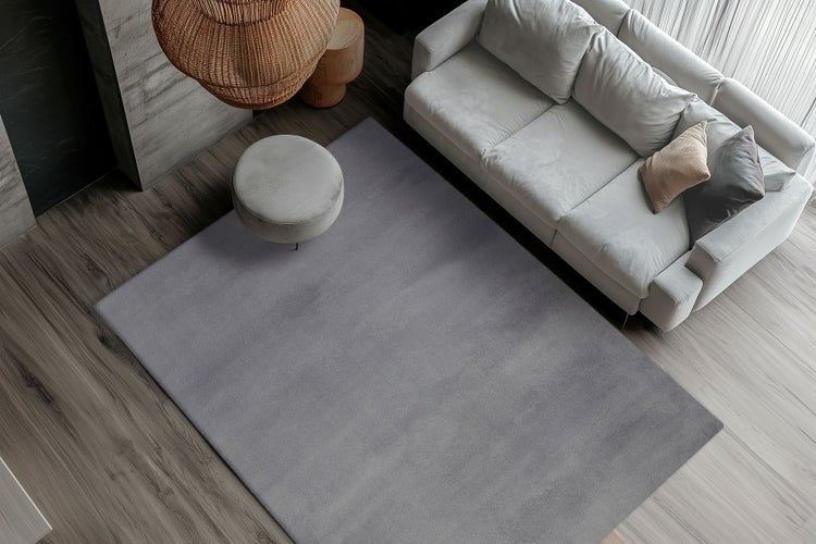 Ein moderner Wohnbereich in Draufsicht mit einem großen rechteckigen Teppich, einem Sofa und einem runden Hocker auf Holzboden.