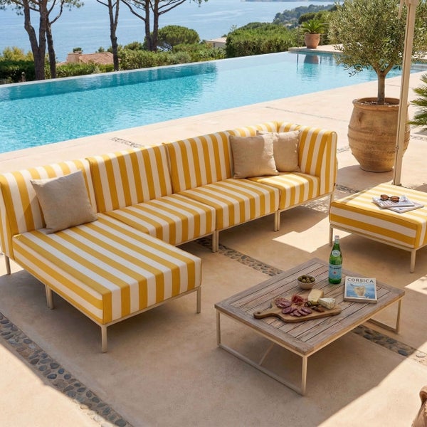 Modulares L-förmiges Garten-Lounge-Set mit gelb-weiß gestreiften Polstern, Holz-Couchtisch und Hocker auf einer hellen Terrasse am Pool.