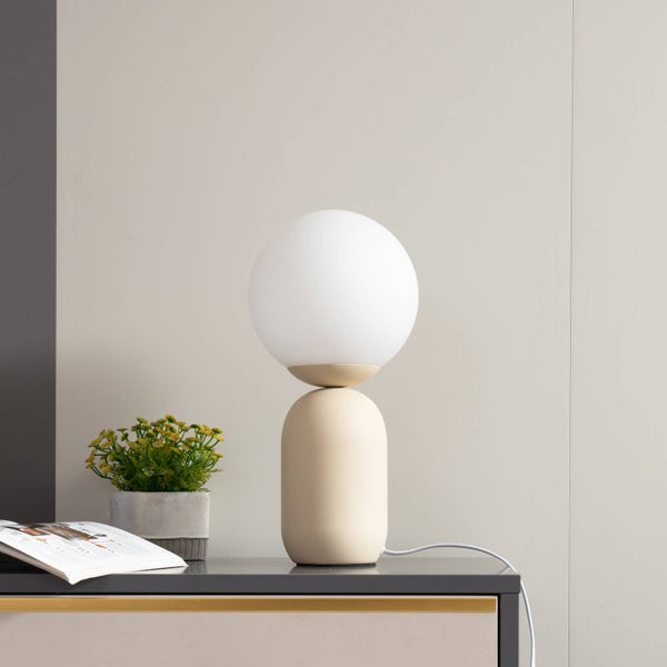 Dekorative Tischleuchte mit runder Glaskugel und beigem Sockel auf einem Nachttisch