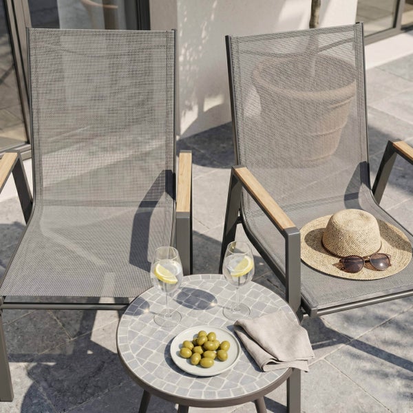 Zwei Gartenstühle mit grauem Netzgewebe und Holzarmlehnen neben einem runden Mosaiktisch auf einer Terrasse.