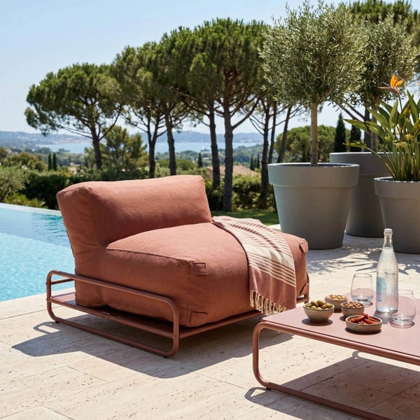 Moderner Outdoor-Loungesessel mit Metallgestell und passendem Beistelltisch auf einer Terrasse am Pool mit Olivenbäumen und Ausblick.