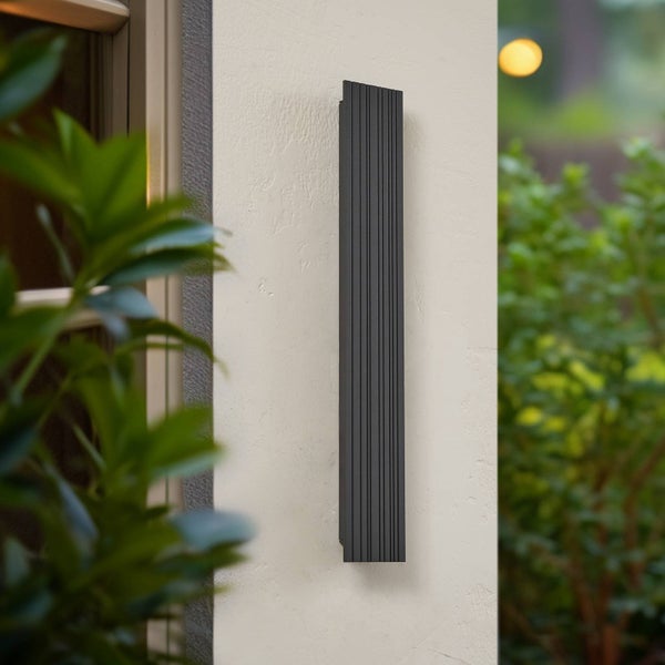 Moderne Außenwandleuchte in Schwarz, vertikale rechteckige Form mit gerippter Oberfläche, montiert an einer Fassade.