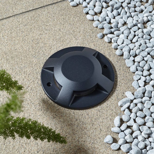 Runde Bodeneinbauleuchte für den Außenbereich, eingebaut in eine Steinfläche neben Zierkies.