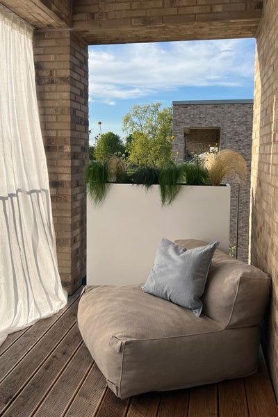 Moderner Balkon mit gepolstertem Sitzsack, Holzboden, weißem Pflanzkübel mit Ziergräsern und Wänden aus hellen Ziegelsteinen.