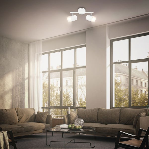 Moderne zweiflammige Deckenleuchte in einem hellen Wohnzimmer mit großen Fenstern, braunen Sofas und einem Couchtisch aus Glas.