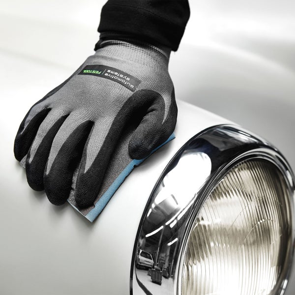 Ein Arbeiter trägt Arbeitshandschuhe und poliert die Karosserie eines Autos.