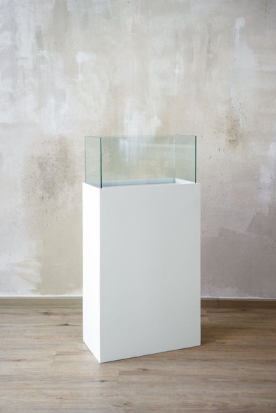 Dekorative Anordnung mit Kerzen und Weihnachtskugeln in einem Glasbehälter auf einer weißen Säule.