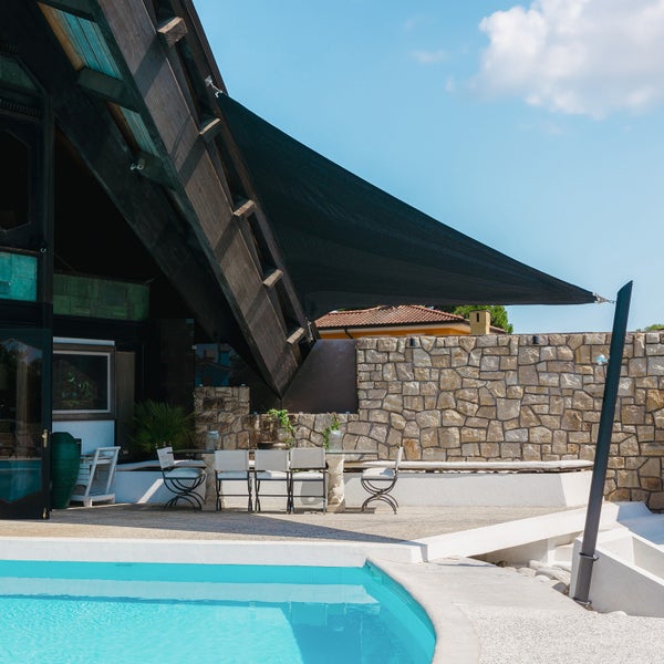 Dunkles dreieckiges Sonnensegel gespannt über eine Terrasse mit Esstisch und Stühlen neben einem Swimmingpool.