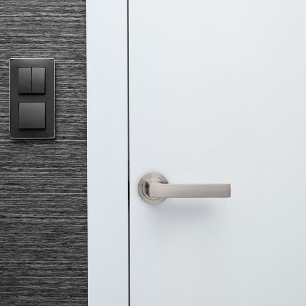 Moderne weiße Zimmertür mit Metalltürdrücker und daneben liegendem Lichtschalter an strukturierter Wand