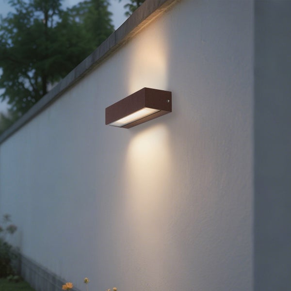 Rechteckige Außenwandleuchte in Rostoptik mit Up-und-Down-Lichteffekt an einer Gartenmauer montiert.