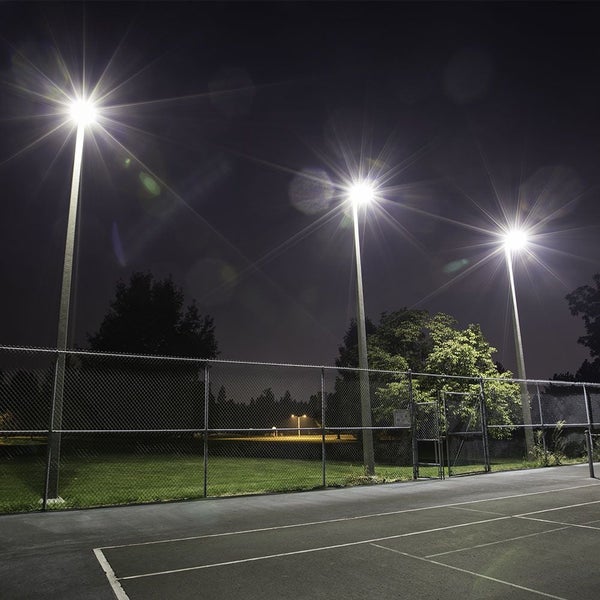 Beleuchteter Tennisplatz bei Nacht mit Zaun