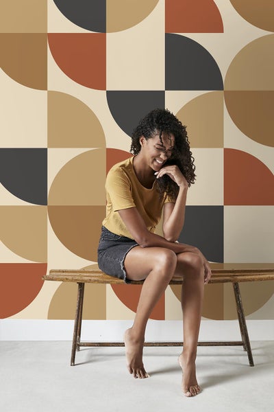 Frau sitzt vor geometrischer Tapete auf einer Holzbank.