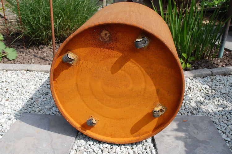 Unterseite eines runden Pflanzkübels aus Metall in Rostoptik mit vier montierten Lenkrollen im Garten.