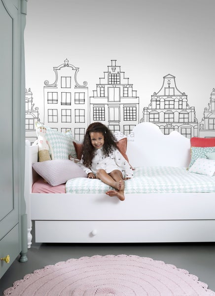 Kinderzimmer mit Bett, Kissen, Teppich und Wandbild mit Häusern