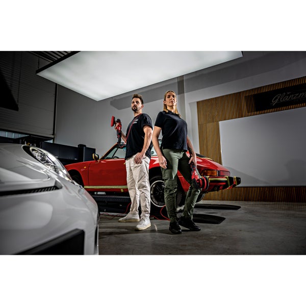 Ein Mann und eine Frau halten jeweils eine FLEX Poliermaschine vor einem roten Oldtimer in einer professionellen Werkstatt.