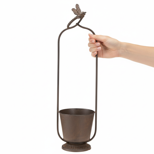 Dekorativer Blumentopf aus Metall mit hohem Bügel und Libellenfigur, in einer Hand gehalten.