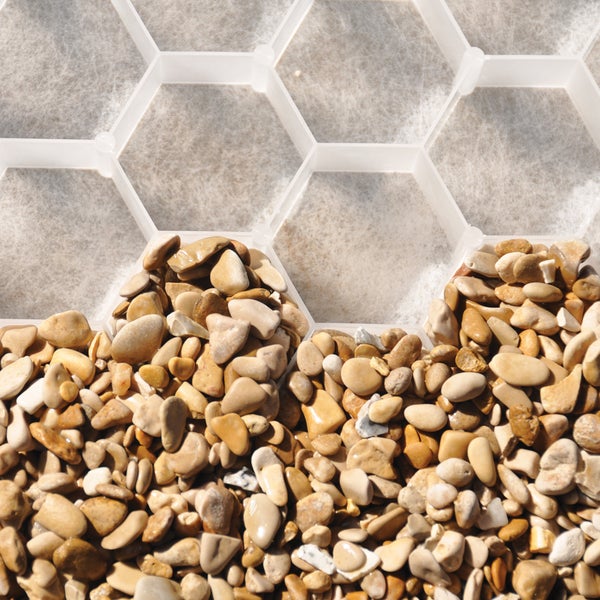 Wabenförmige Kiesstabilisierung aus Kunststoff, teilweise befüllt mit beigefarbenen Kieselsteinen auf hellem Vliesuntergrund.