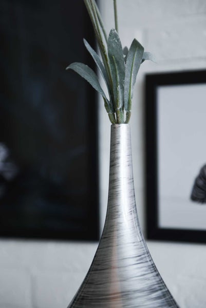 Schlanke Vase in gebürsteter Metalloptik mit künstlichen grünen Blättern in einer modernen Inneneinrichtung.