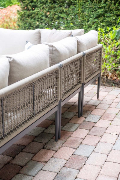 Detailansicht eines Gartensofas mit Seilbespannung, dunklem Metallgestell und hellen Polstern auf einer Terrasse.